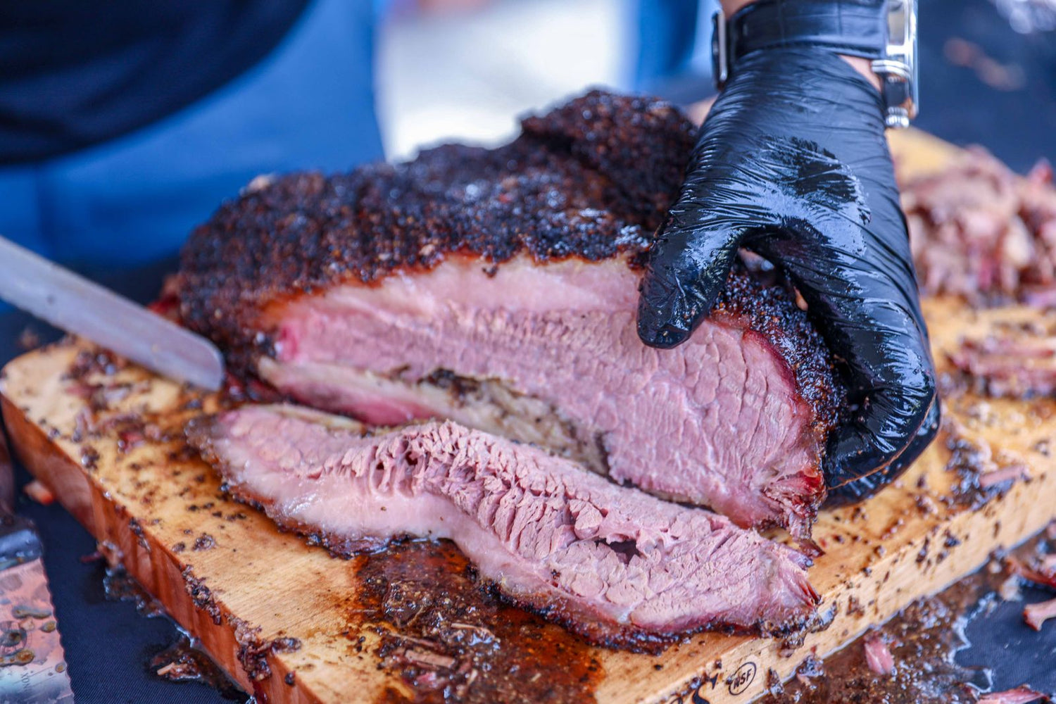 Brisket ahumado con su costra oscura, cortado en tajadas sobre una tabla